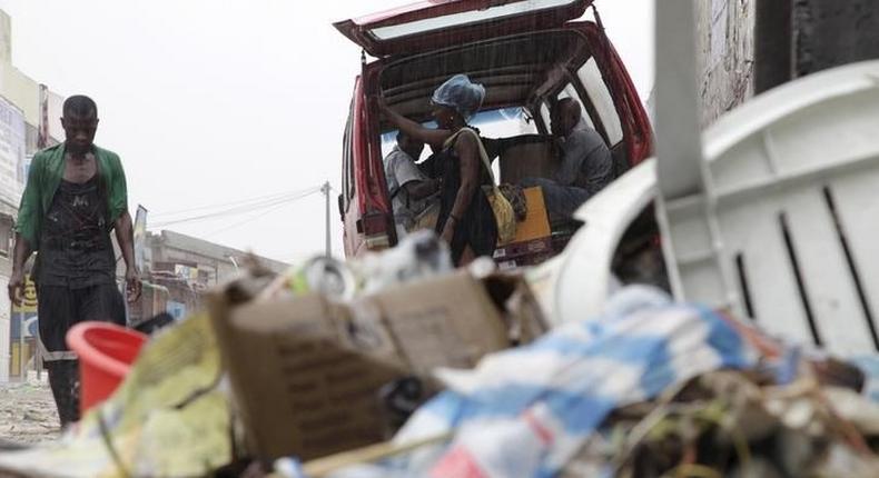 People walk past a pile of garbage along a street during rainfall, in Luanda, Angola, in this picture taken February 10, 2016. 