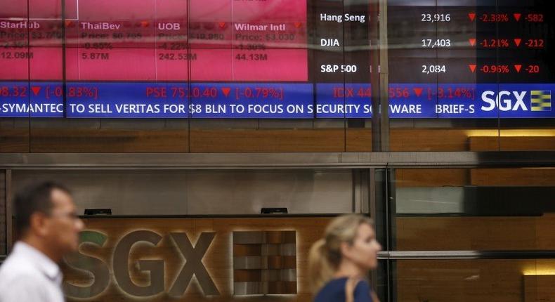 People pass a stock board showing stocks in red outside the Singapore Exchange in the central business district in Singapore August 12, 2015. 