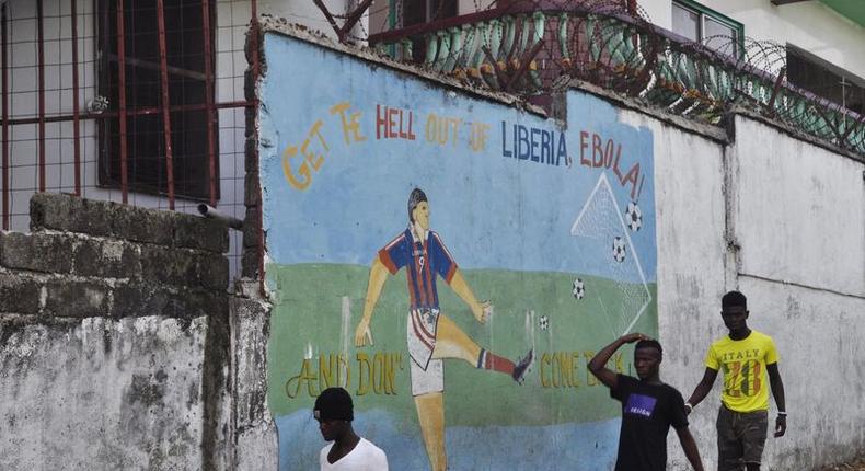 Men walk by a mural that reads Get the hell of Liberia, Ebola! And don't come back in Monrovia, Liberia, April 1, 2016. REUTERS/James Giahyue