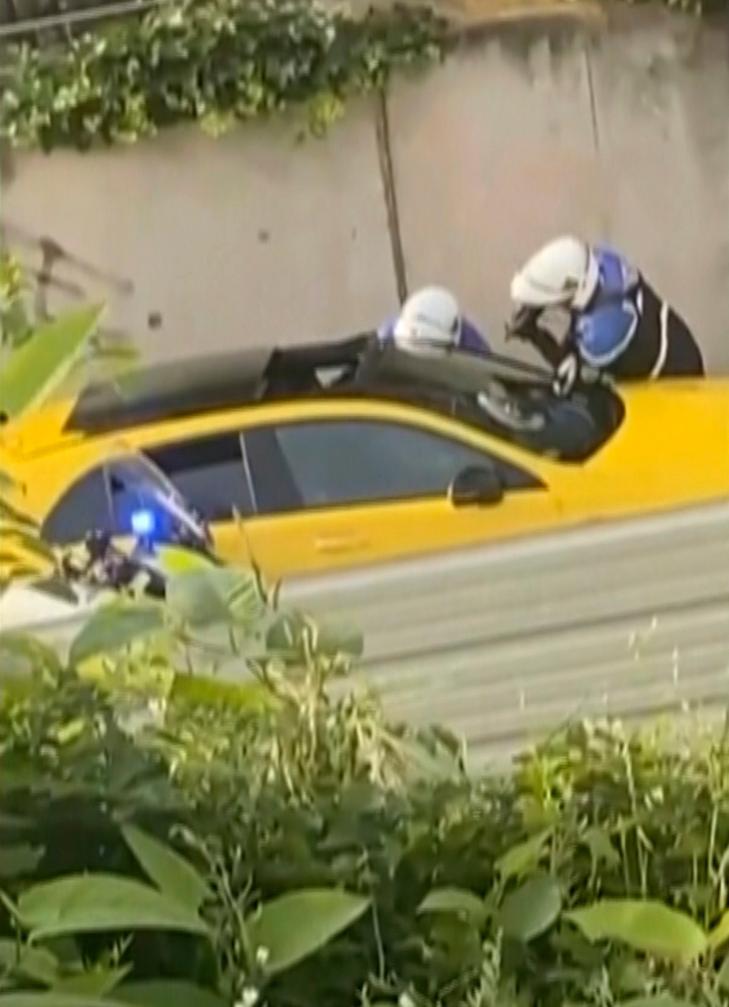 Na snímke z videa dvaja policajti sa pýtajú mladého vodiča, jeden z nich mieri zbraňou na okno žltého auta, ktorého zastavili počas dopravnej kontroly.