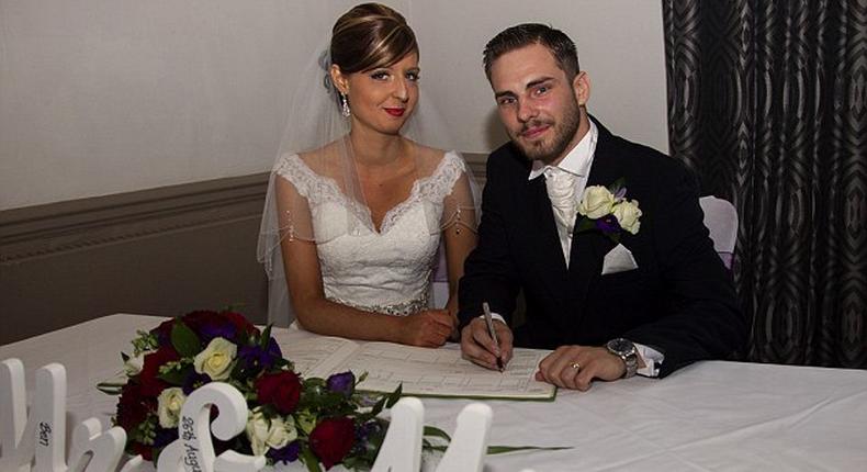 The couple pose for the camera while signing the wedding register 