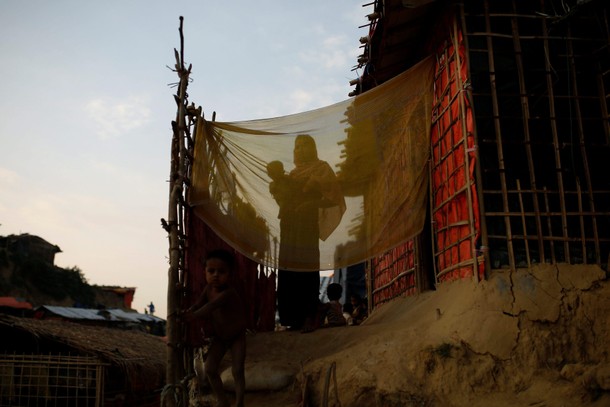 A Rohingya refugee woman holds her baby as she stands outside her temporary shelter at the Balukhali