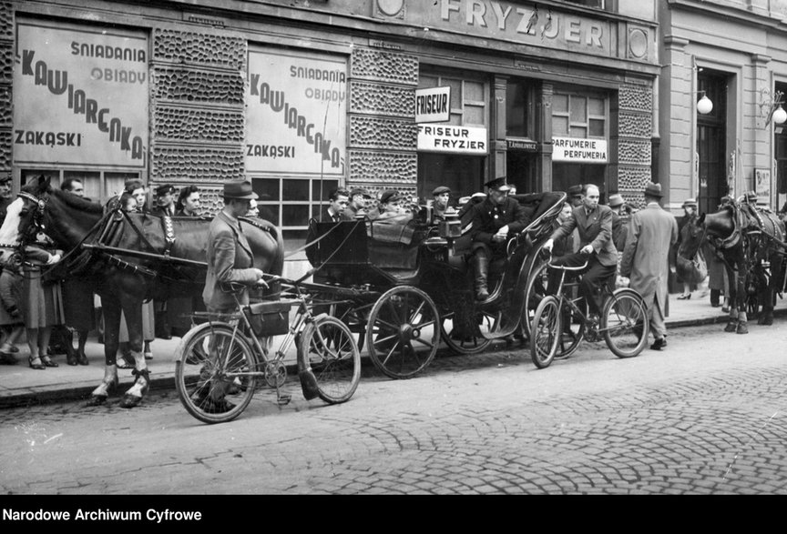 Warszawa 1940 r. Dorożka, rowerzyści i ludność cywilna przed zakładem fryzjerskim i kawiarnią przy ul. Złotej 8.