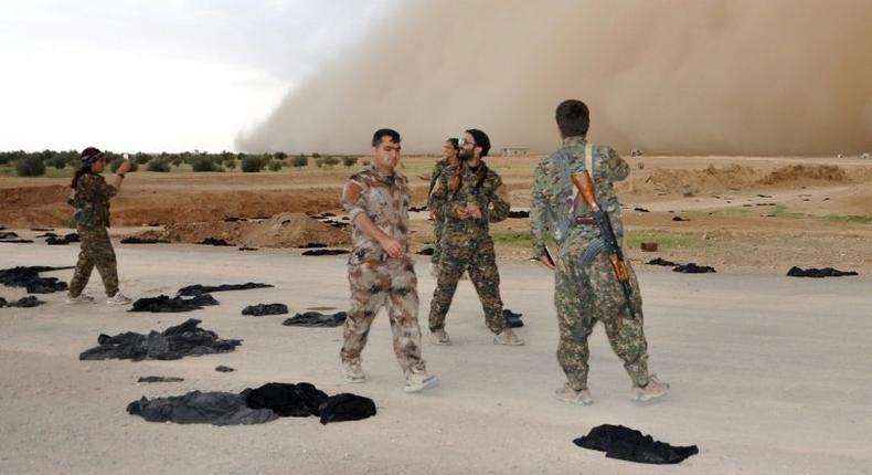 Fighters from the Syrian Democratic Forces (SDF) walk along a road dotted with black veils ditched by women after they crossed over from Islamic State group territory near Tishreen Farms, on the northern outskirts of Raqa on May 2, 2017