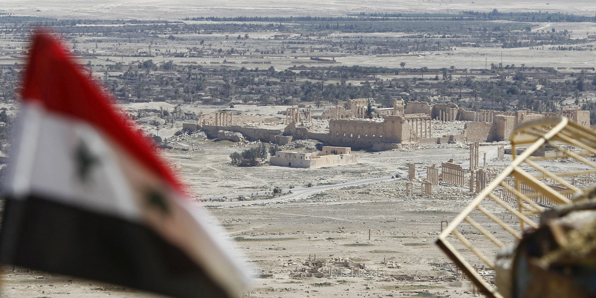 A Syrian national flag flutters as the ruins of the historic city of Palmyra are seen in the background, in Homs Governorate, Syria April 1, 2016.