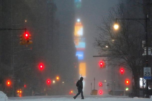 Times Square is seen in the background as a man walks along West 59th street in falling snow in Manh