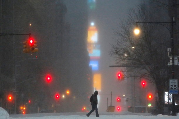 Times Square is seen in the background as a man walks along West 59th street in falling snow in Manh