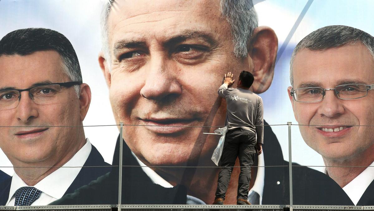 A labourer works on hanging up a Likud election campaign banner depicting Israeli Prime Minister Ben