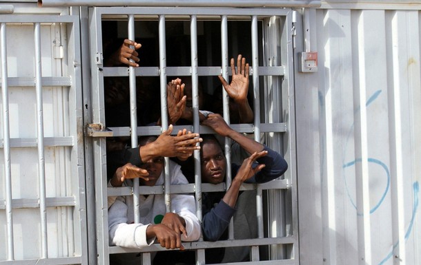 Illegal migrants, who have been detained after trying to get to Europe, look out of barred door of a