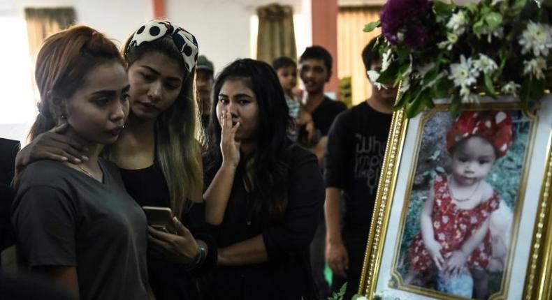 Jiranuch Trirat (L) is comforted by friends as she looks at a photograph of her 11-month-old daughter Natalie during funeral rites at a temple in Phuket, Thailand