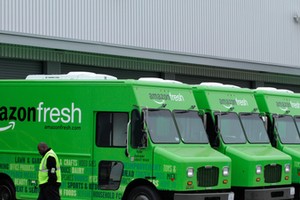 A worker walks past Amazon Fresh delivery vans parked at an Amazon Fresh warehouse in Inglewood