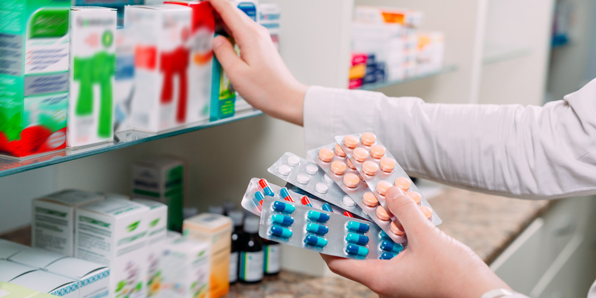 Pharmacist holding medicine box and capsule packs in pharmacy drugstore.