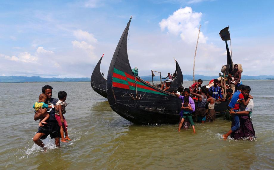 Smoke is seen on Myanmar's side of border as a Rohingya refugee men carry children from a boat after