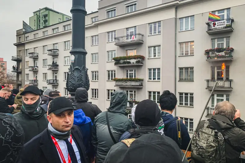 Organizator Marszu Niepodległości Robert Bąkiewicz na tle płonącego od racy mieszkania 