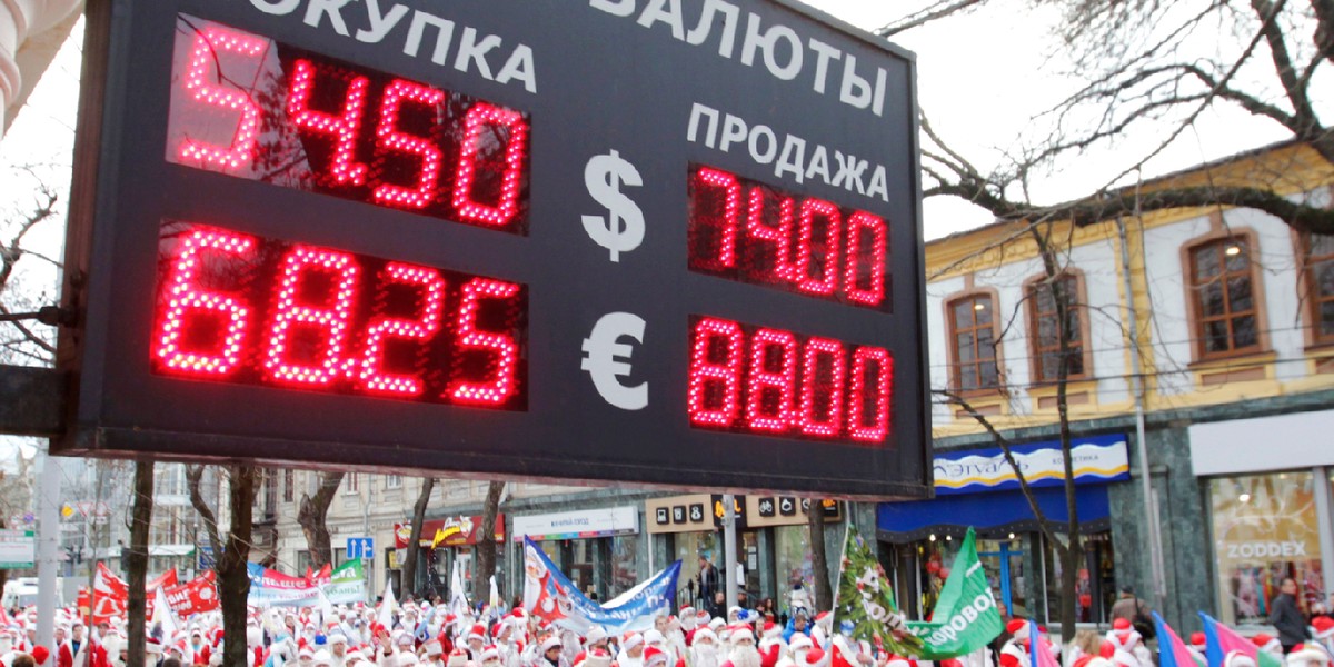 People dressed as Father Frost, the equivalent of Santa Claus, walk past a board showing currency exchange rates, during a parade in the Russian southern city of Krasnodar December 20, 2014.