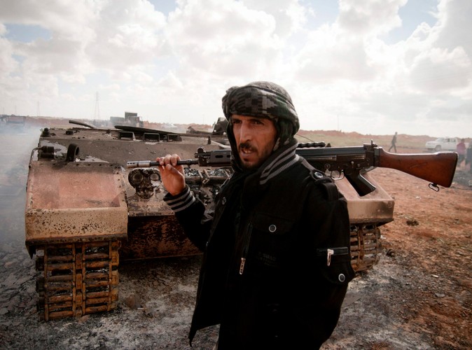 Rebeliant przed spalonym czołgiem, należącym do sił Muammara Kadafiego, zniszczonym podczas francuskiego nalotu 25 km od Bengazi