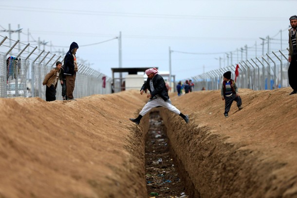 Displaced people who fled from the clashes in Mosul jump across a ditch at Khazer camp