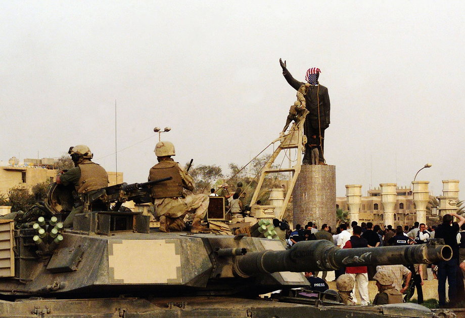 Żołnierz piechoty marynarki wojennej USA zasłania głowę pomnikowi Saddama Husajna 9 kwietnia 2003 roku
