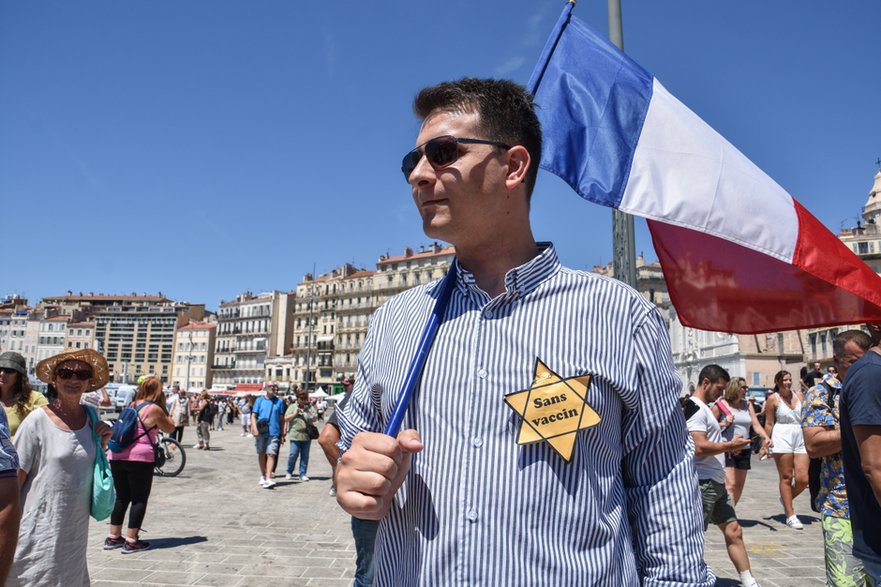 Protesty w Marsylii przeciwko przywilejom dla zaszczepionych, lipiec 2021 r. Mężczyzna na zdjęciu ma Gwiazdę Dawida z napisem „Bez szczepionki”, która przypomina gwiazdy noszone przez Żydów w gettach podczas Holocaustu