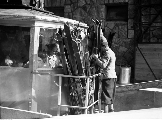 Pasażerowie w wagoniku kolejki linowej. Transport nart w platformie przymocowanej na zewnątrz wagonika