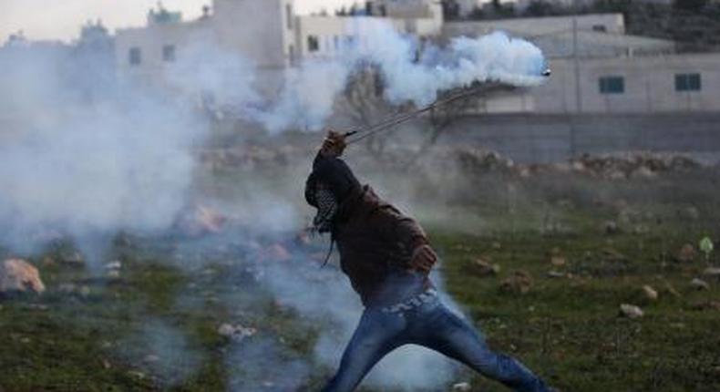 A Palestinian protester returns a tear gas canister fired by Israeli troops during clashes in the West Bank village of Silwad, near Ramallah December 26, 2015.