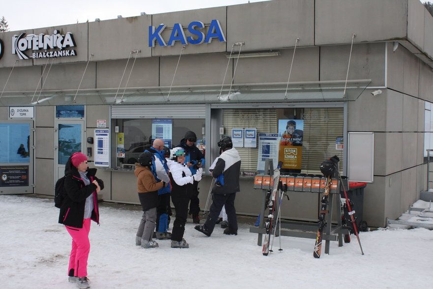 Turyści przed kasą biletową kupują karnety na wyciąg narciarski.