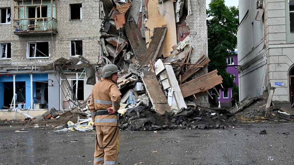Ukraiński ratownik stoi obok budynku częściowo zniszczonego po rosyjskim ataku rakietowym w Charkowie