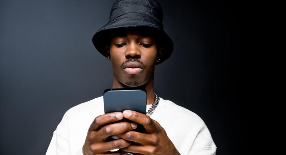 Portrait of handsome young man wearing white sweatshirt and black bucket hat, using mobile phone. Studio shot on black background. 