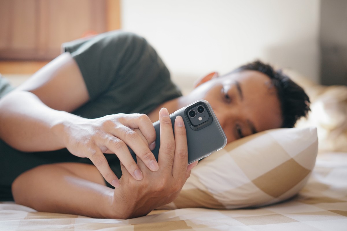Chłopie leży w łóżku i patrzy w telefon