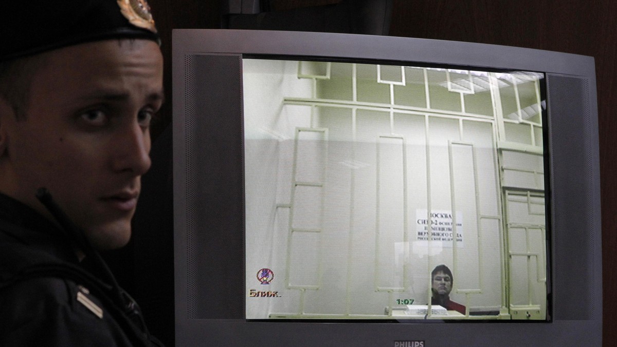 A bailiff stands next to a screen with a live broadcast of a court hearing an appeal by an oppositio