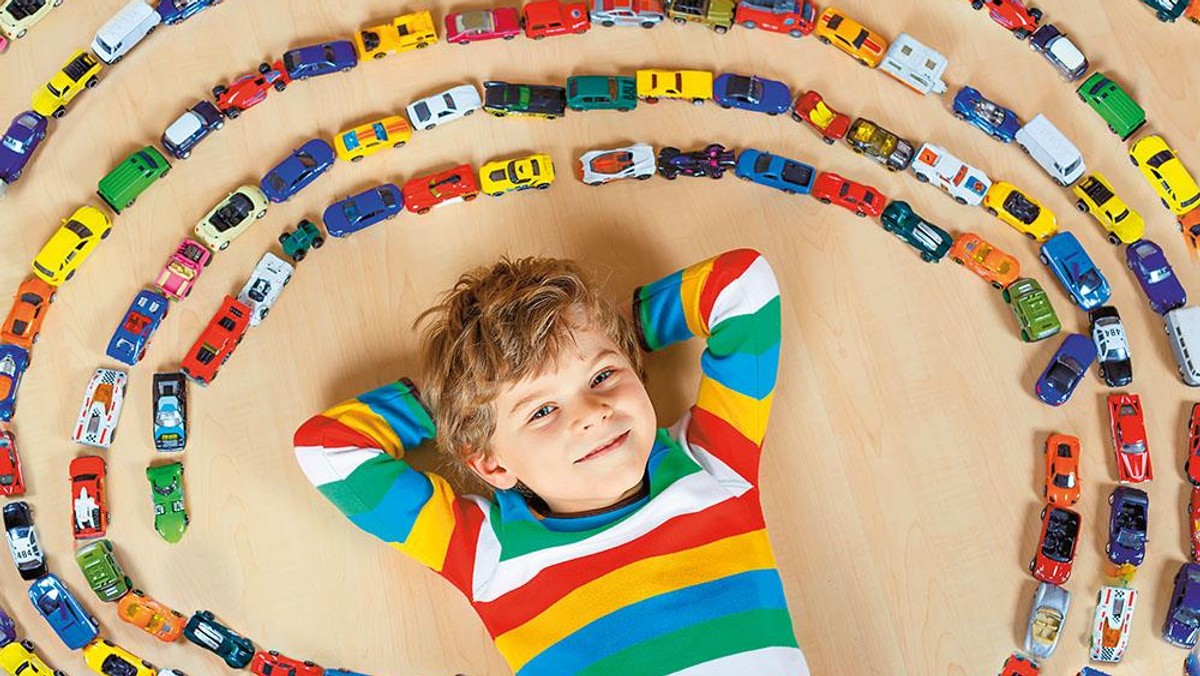 Cute little blond kid boy playing with lots toy cars