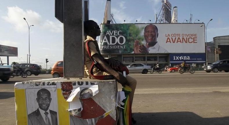 A student sits next to campaign posters of independent candidate Kouadio Konan Bertin, with a campaign billboard Ivory Coast President Alassane Ouattara seen in the background, ahead of the October 25 presidential election, in Abidjan October 21, 2015. The billboard reads, Ivory Coast, advance. REUTERS/Luc Gnago