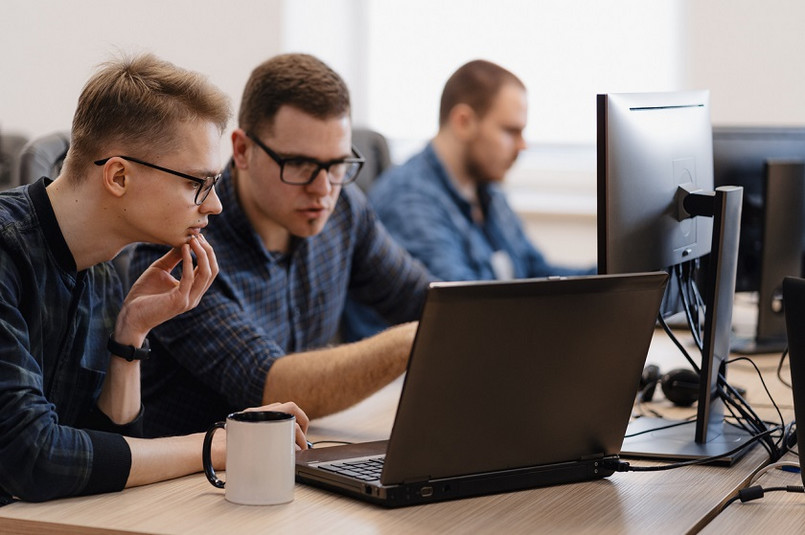 Full concentration at work. Group of young business people working and communicating while sitting at the office desk together with colleagues sitting in the background