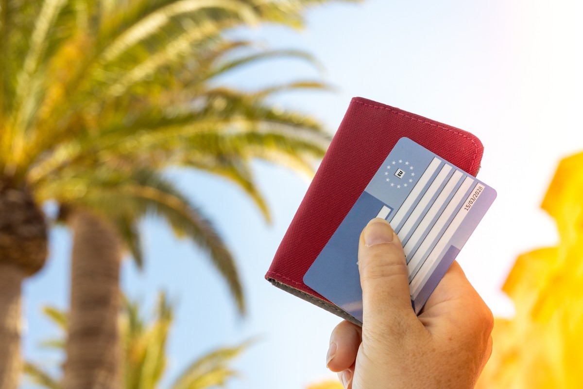 Turysta trzymający w ręce kartę EKUZ na tle palm.