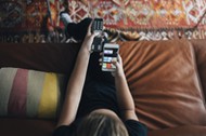 High angle view of teenage girl using phone app and remote control while sitting on sofa watching TV