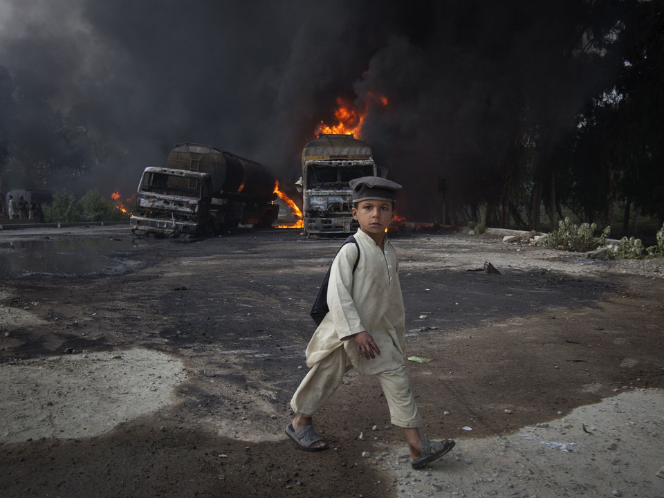 A school boy, wearing a backpack, walks past burning fuel tankers along the GT road in Nowshera, Pakistan