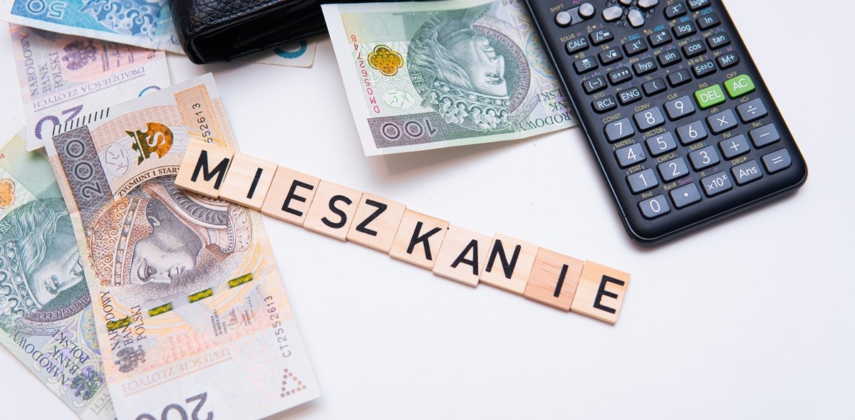 Klocki z napisem mieszkanie leżące na banknotach obok kalkulatora
