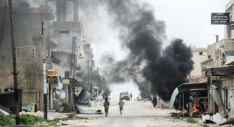 Fighters run past smoke from a burning tyre meant to disrupt warplanes in the Syrian town of Tayyibat al-Imam in the countryside of Aleppo province on March 22, 2017
