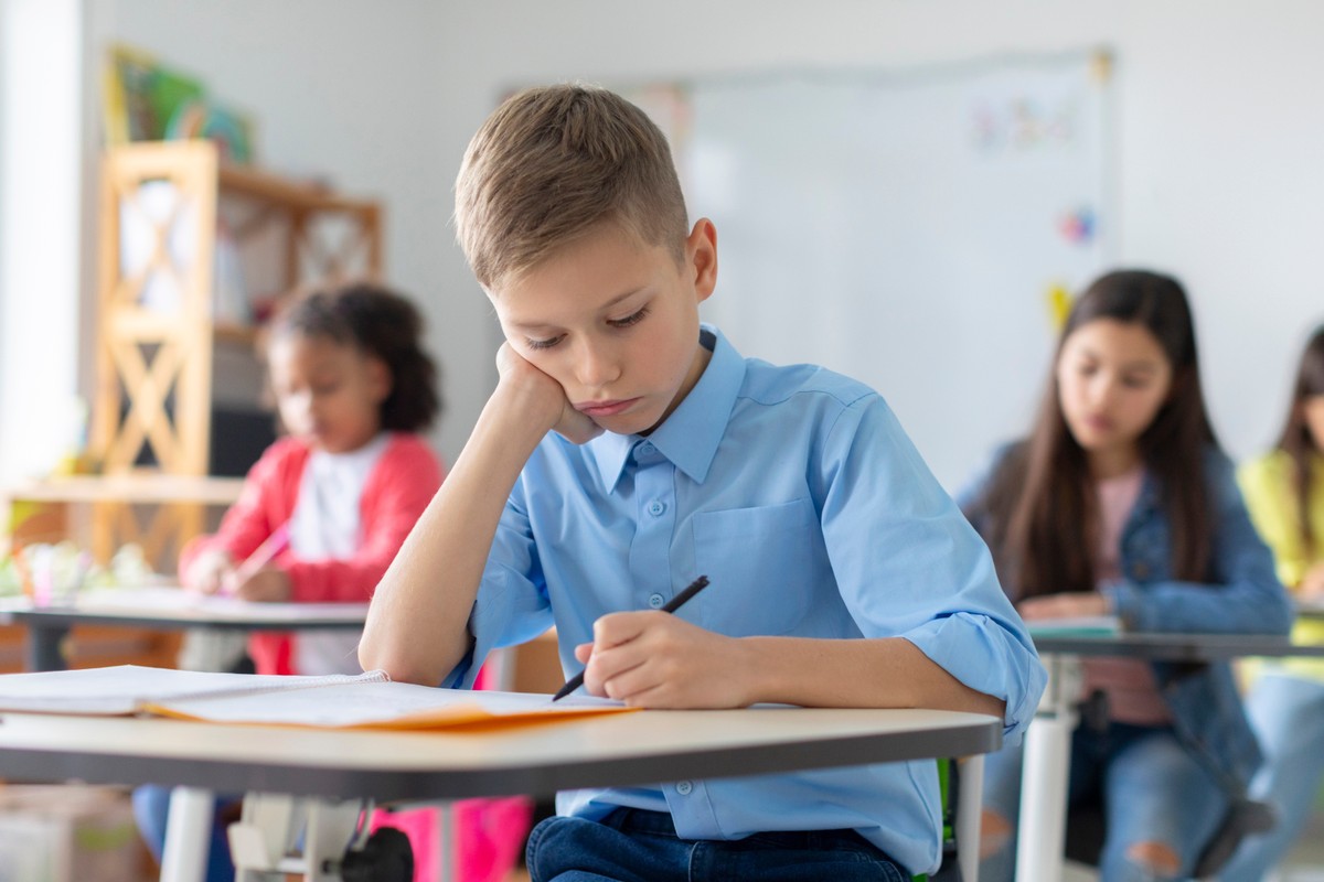 Sad,Schoolboy,Sitting,At,Desk,,Looking,Down,,Leaning,Head,On