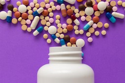 Capsules spilling out of white bottle. Violet background.