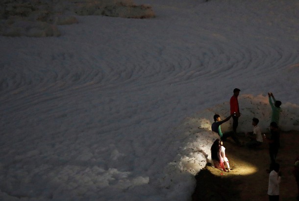 People get their picture taken in front of the foam covering the polluted Yamuna river in New Delhi