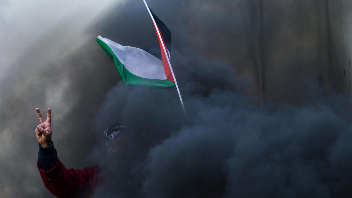 Protester holds a Palestinian flag as smoke rises from a burning tyre during clashes with Israeli tr