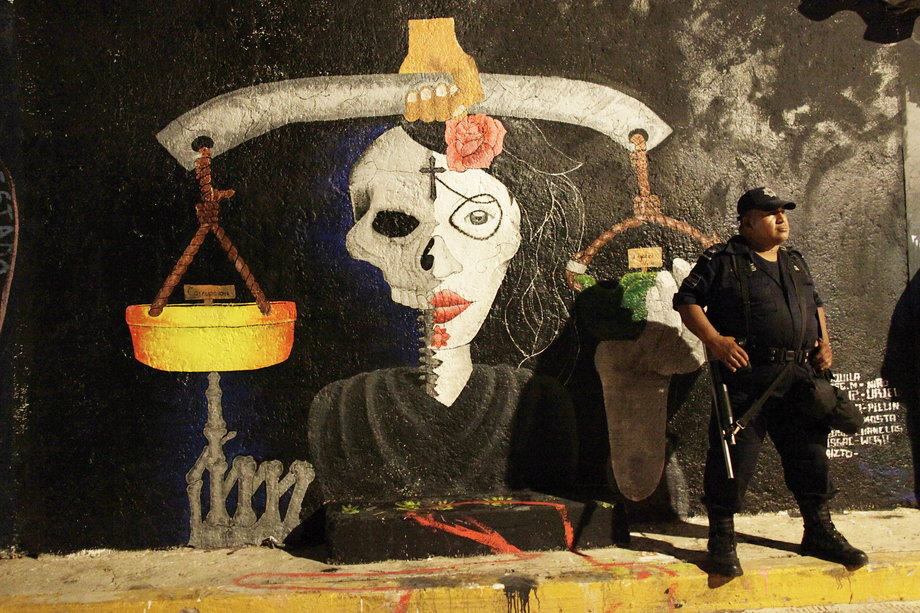 A policeman stands in front of a mural painted by students to demand the government justice for the 43 missing students from the Ayotzinapa Teacher Training College Raul Isidro Burgos, in the town of Tixtla, in the southern state of Guerrero October 31, 2014.
