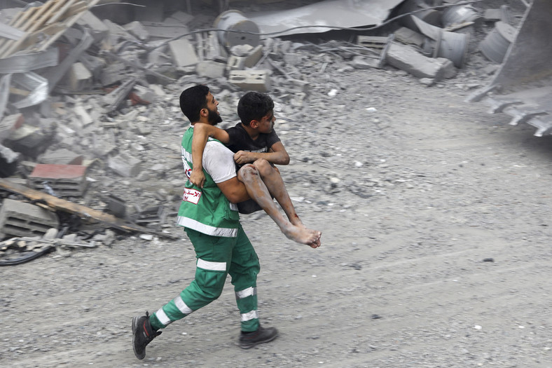 Członek palestyńskiej obrony cywilnej niesie rannego chłopca uratowanego spod gruzów domu. 10 października 2023 r.