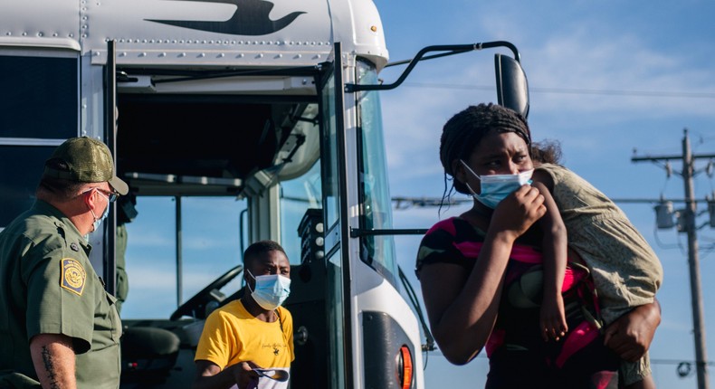 Migrants exit a Border Patrol bus and prepare to be received by the Val Verde Humanitarian Coalition after crossing the Rio Grande on September 22, 2021 in Del Rio, Texas.
