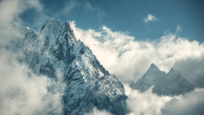 Manaslu mountain with snowy peak in clouds in sunny bright day in Nepal. Landscape with high snow covered rocks and blue cloudy sky. Beautiful nature. Fairy scenery. Aerial view of Himalayan mountains