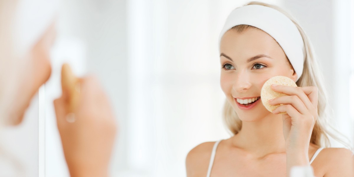 young woman washing face with sponge at bathroom