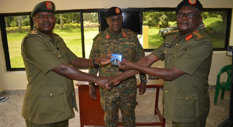Lt Col Moses Kaggwa recieves office stamps from Col Tom Musoke as the 4Inf Division Commander looks on
