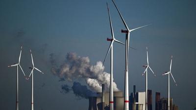 Wind turbines spin in front of a coal-fired power plant operated by German energy giant RWE. The company is burning more coal in response to the global energy crisis but pledged to be carbon neutral by 2040.Ina Fassbender/AFP