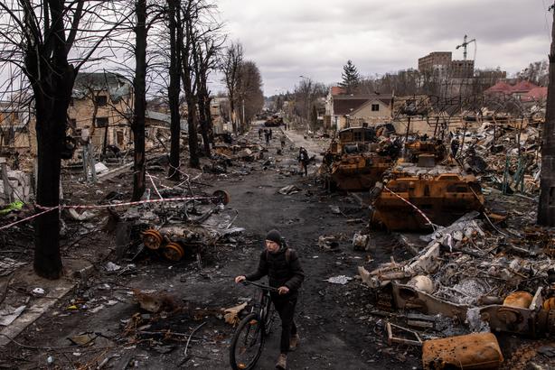 A man pushes his bike through debris and destroyed Russian military vehicles on a street on April 06, 2022 in Bucha, Ukraine.